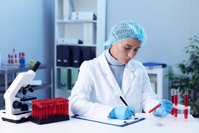 Photo of Laboratory testing. Doctor with blood sample taking notes at table indoors