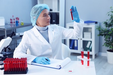 Photo of Laboratory testing. Doctor holding test tube with blood sample at table indoors