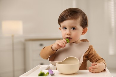 Cute little baby eating healthy food from bowl in high chair at home, space for text