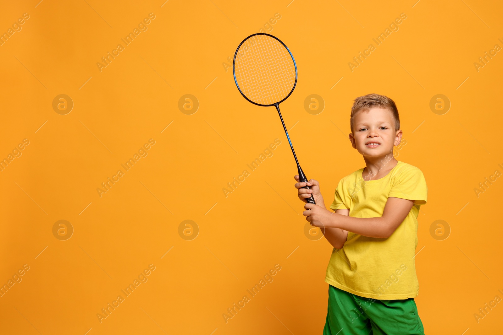 Photo of Little boy with badminton racket on orange background, space for text