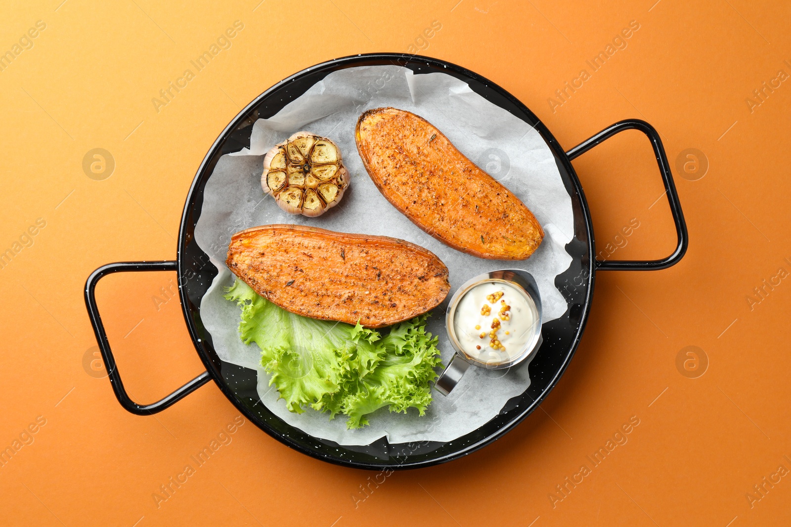 Photo of Tasty cooked sweet potato served in baking dish on orange table, top view