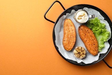 Photo of Tasty cooked sweet potato served in baking dish on orange table, top view. Space for text