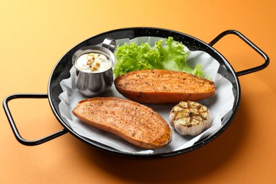 Photo of Tasty cooked sweet potato served in baking dish on orange table