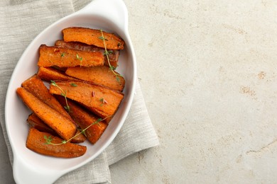 Photo of Pieces of tasty cooked sweet potato with microgreens in baking dish on light textured table, top view. Space for text