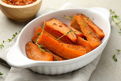 Photo of Pieces of tasty cooked sweet potato in baking dish with microgreens on light textured table, closeup