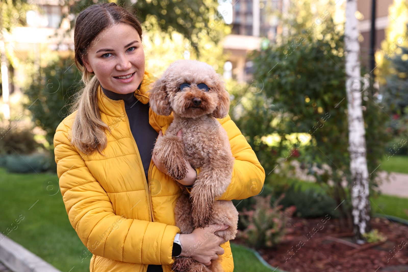 Photo of Woman with cute Toy Poodle dog in sunglasses outdoors