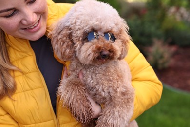 Photo of Woman with cute Toy Poodle dog in sunglasses outdoors