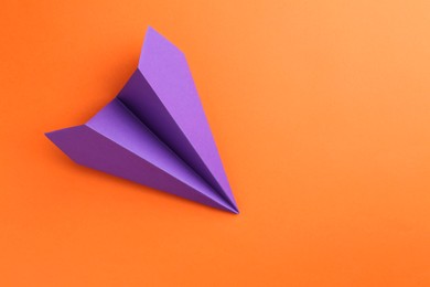 Photo of One handmade violet paper plane on orange background, top view. Space for text