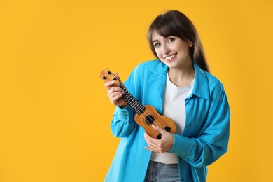 Happy woman playing ukulele on orange background, space for text