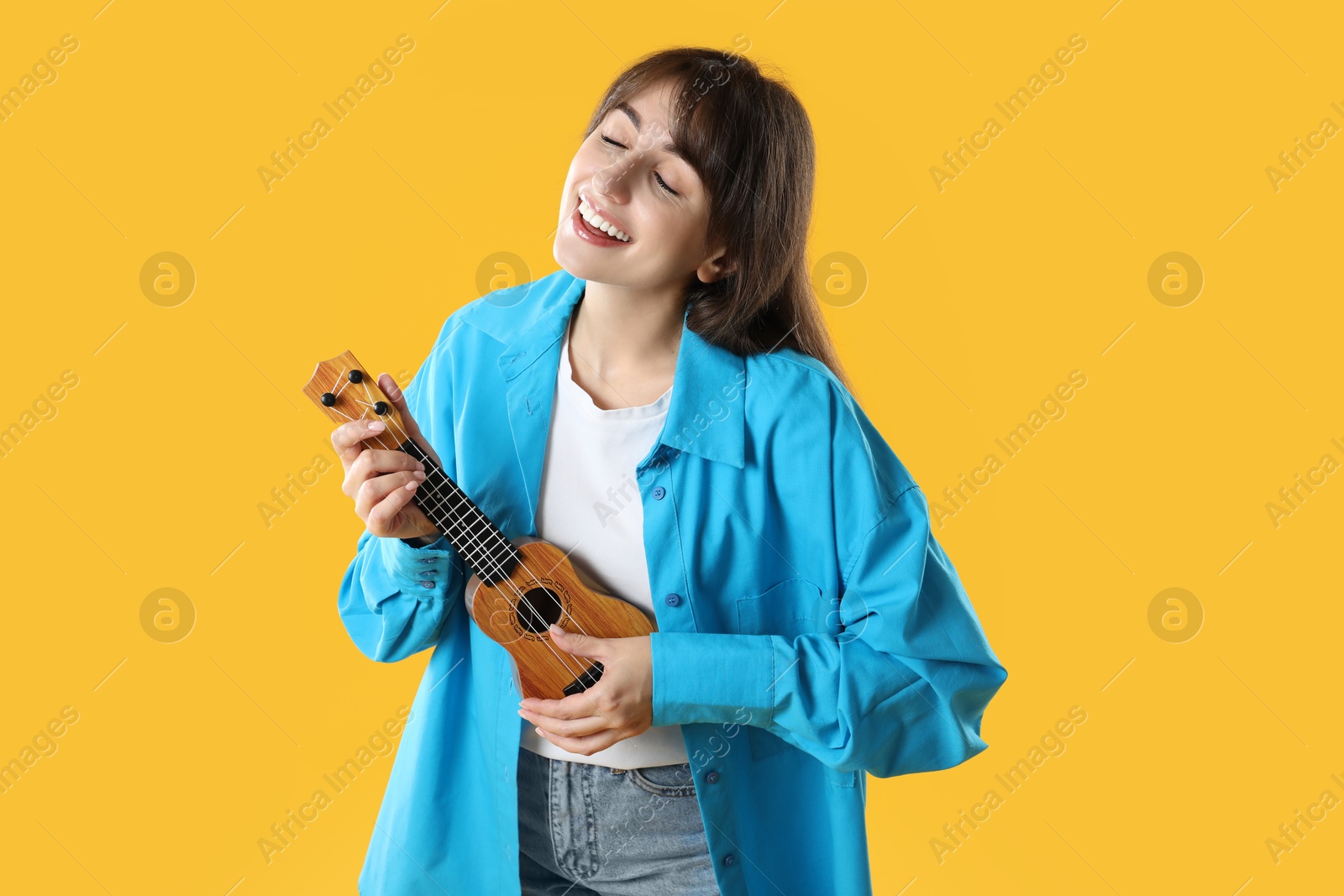 Photo of Happy woman playing ukulele on orange background