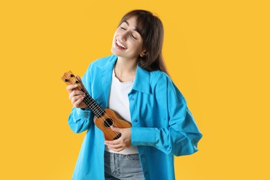 Happy woman playing ukulele on orange background