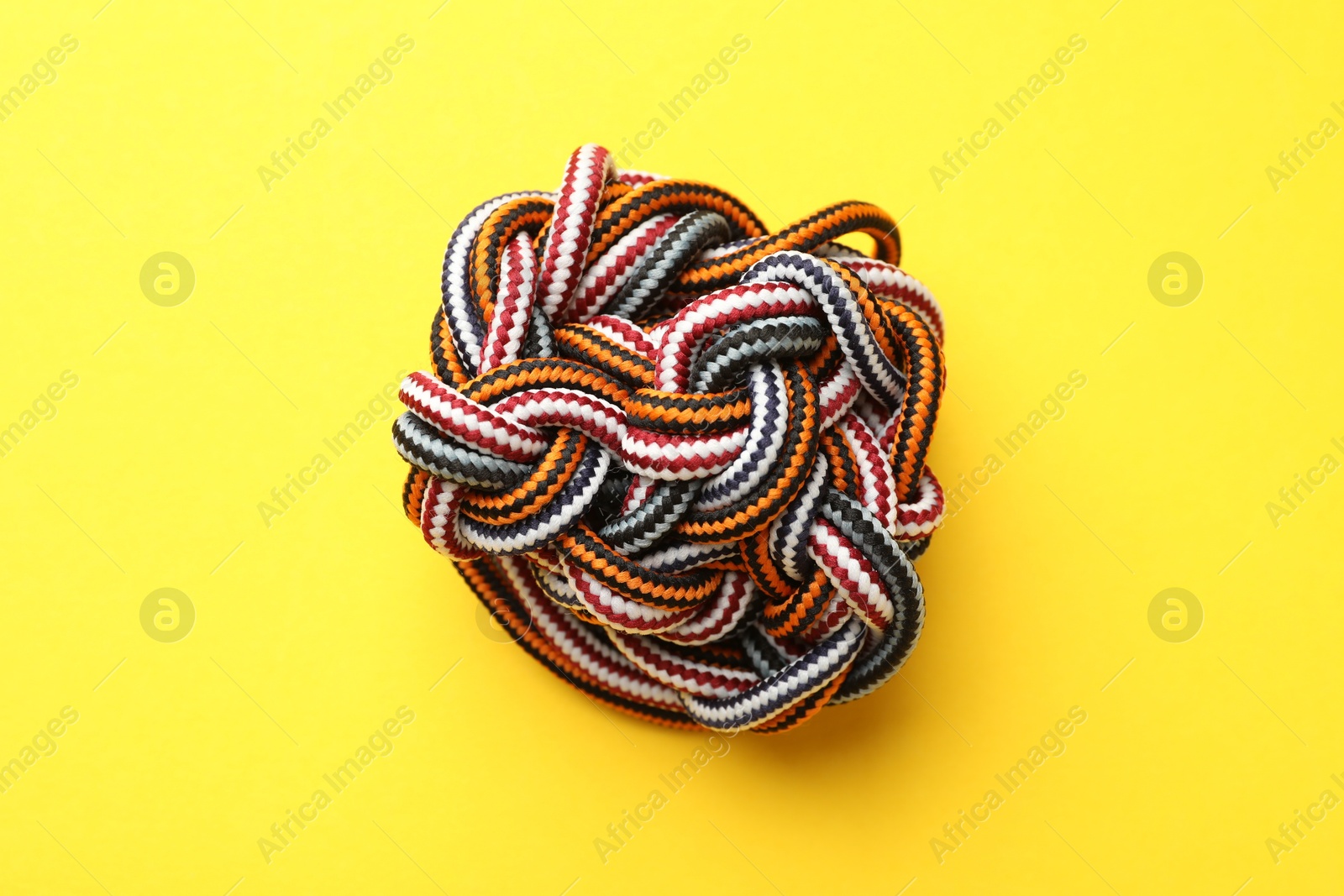 Photo of Colorful ropes tied together on yellow background, top view. Unity concept