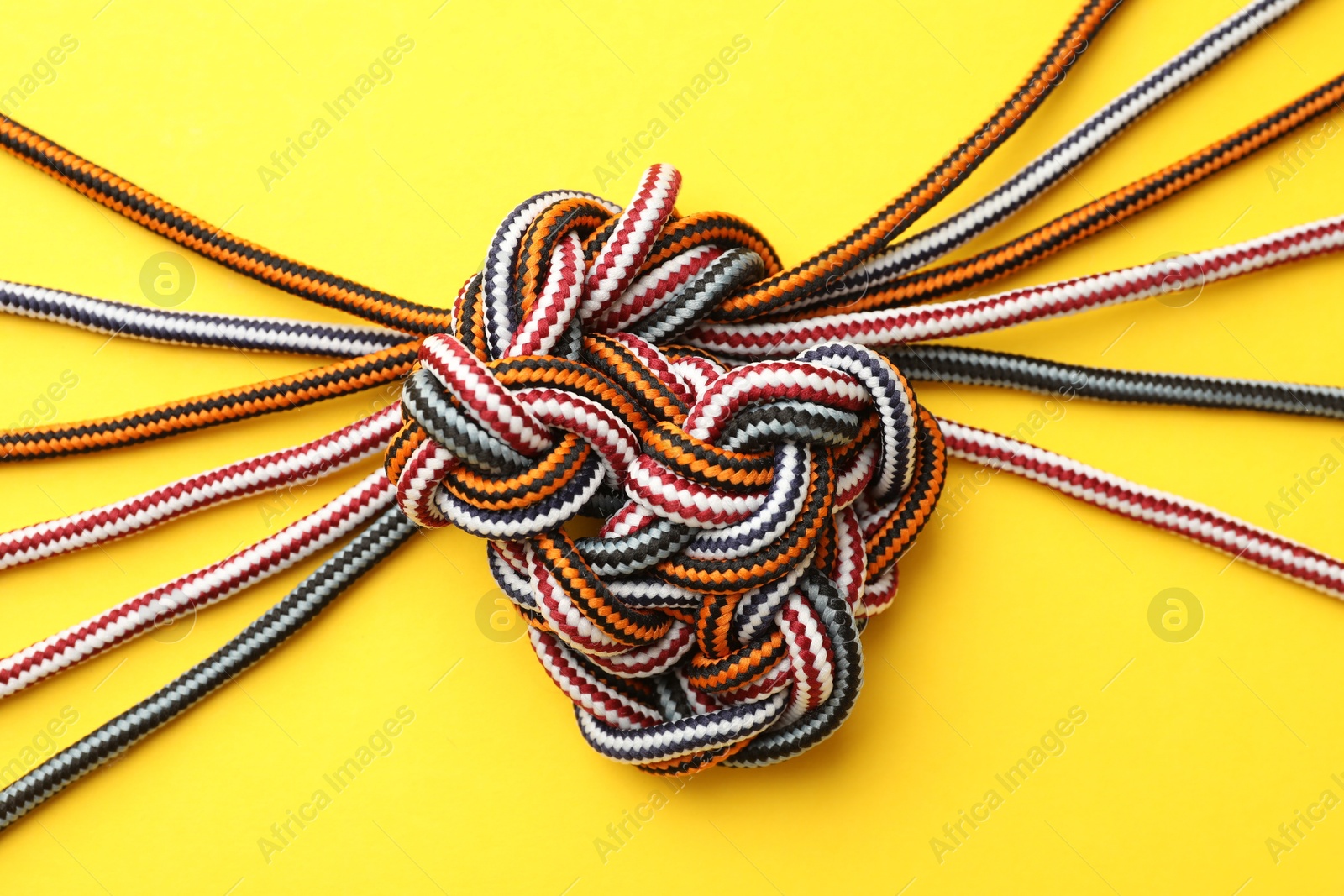 Photo of Braided colorful ropes on yellow background, top view. Unity concept