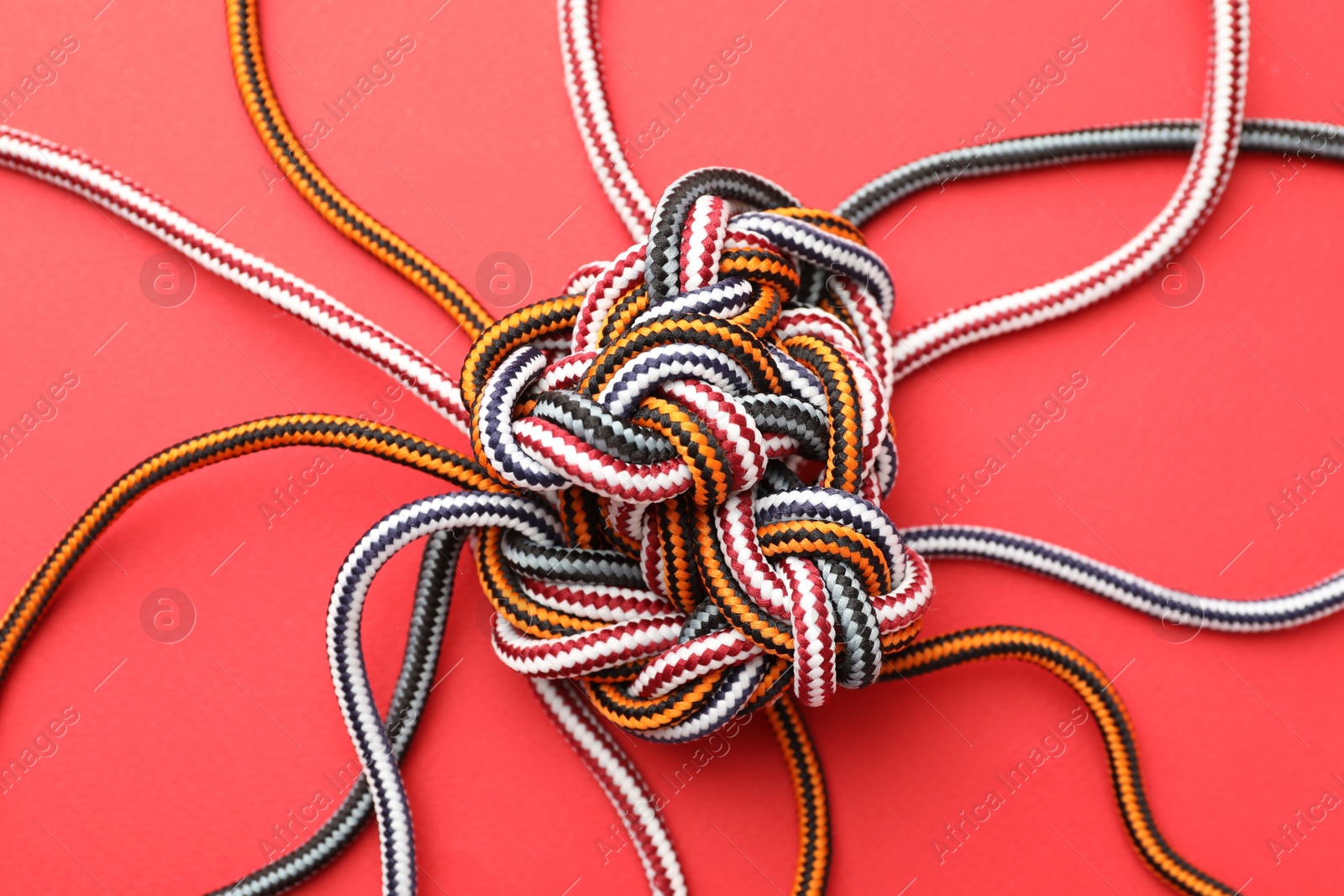 Photo of Braided colorful ropes on red background, top view. Unity concept