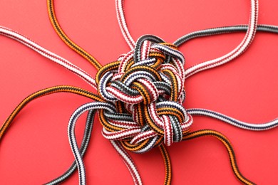 Photo of Braided colorful ropes on red background, top view. Unity concept