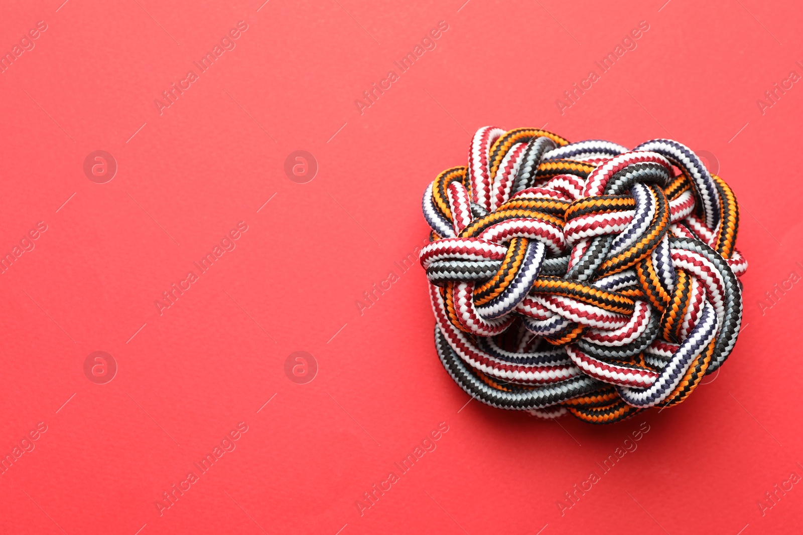 Photo of Colorful ropes tied together on red background, top view with space for text. Unity concept