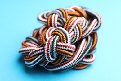 Photo of Colorful ropes tied together on light blue background, closeup. Unity concept