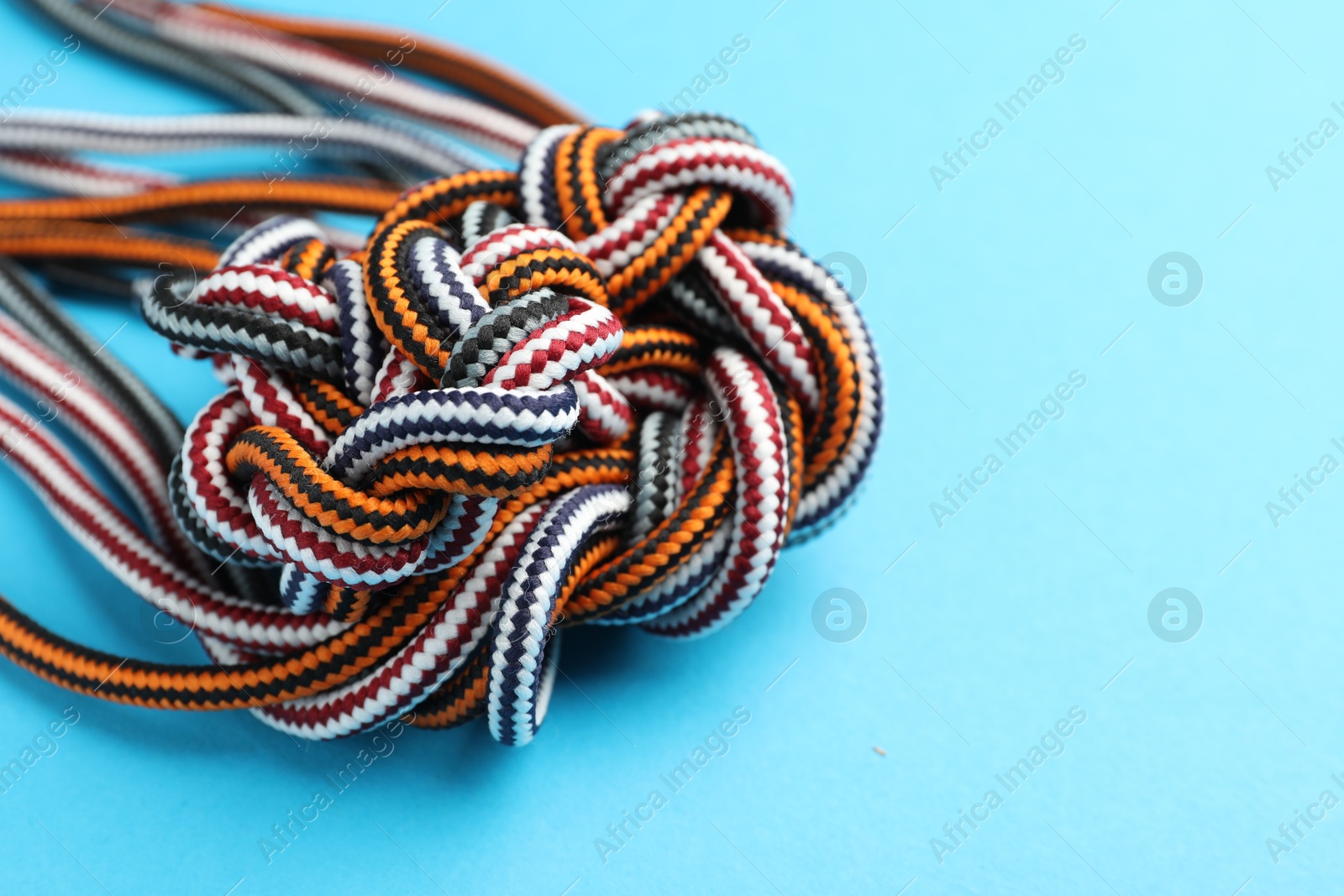 Photo of Colorful ropes tied in knot on light blue background, closeup with space for text. Unity concept