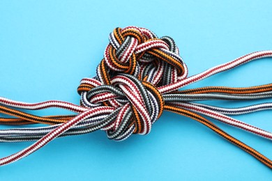 Photo of Colorful ropes tied in knot on light blue background. Unity concept