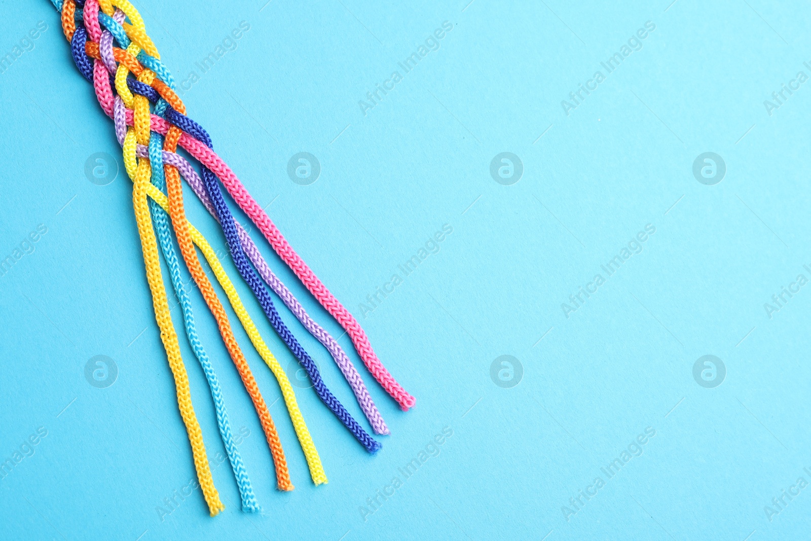 Photo of Braided colorful ropes on light blue background, top view with space for text. Unity concept