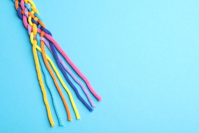 Photo of Braided colorful ropes on light blue background, top view with space for text. Unity concept