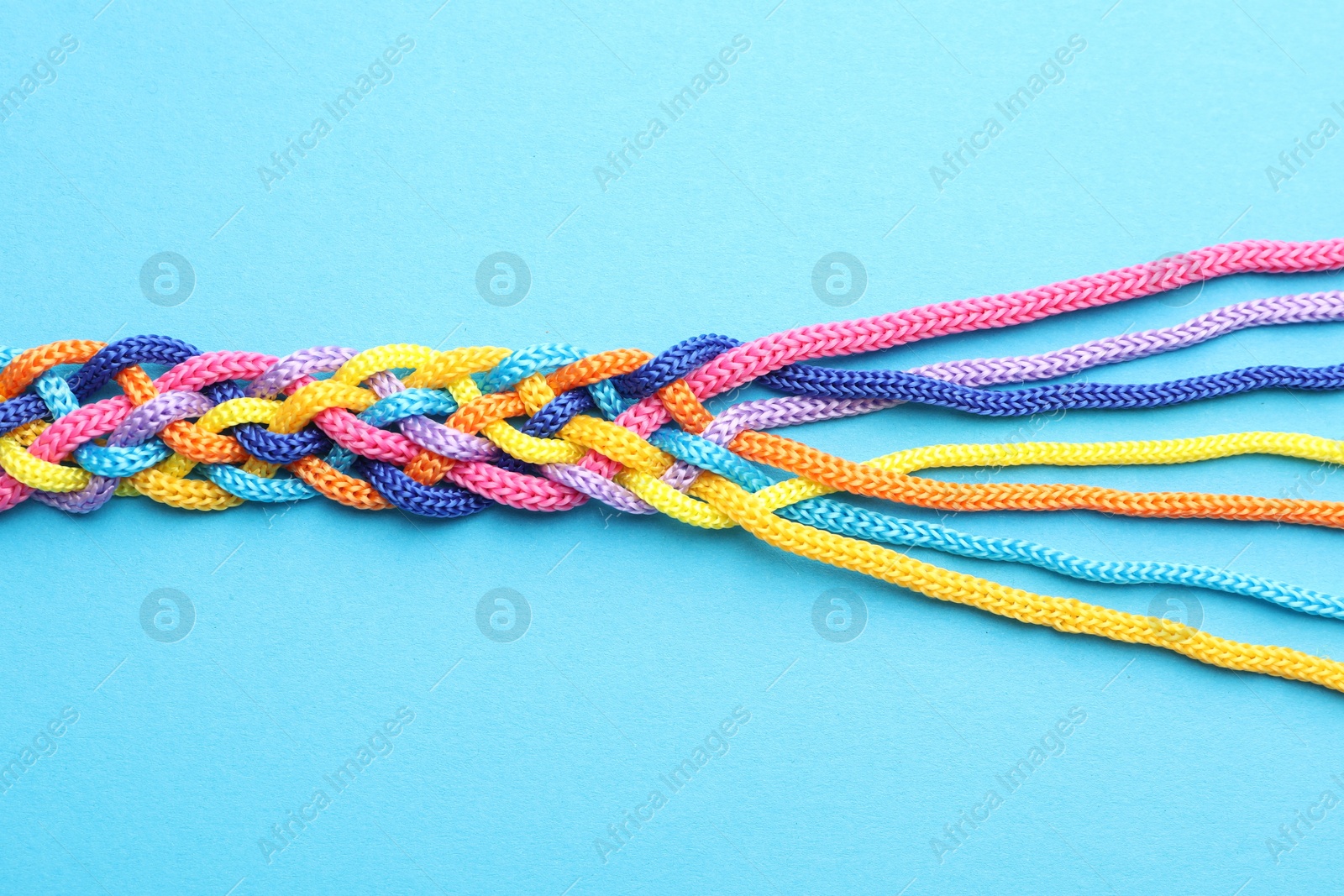 Photo of Braided colorful ropes on light blue background, top view. Unity concept