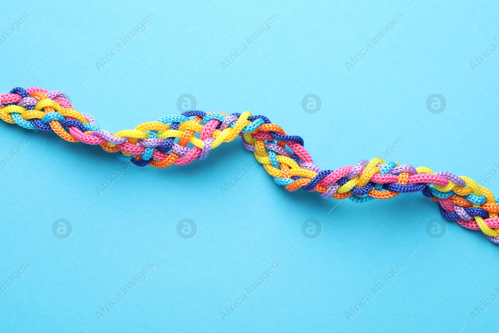 Photo of Braided colorful ropes on light blue background, top view. Unity concept