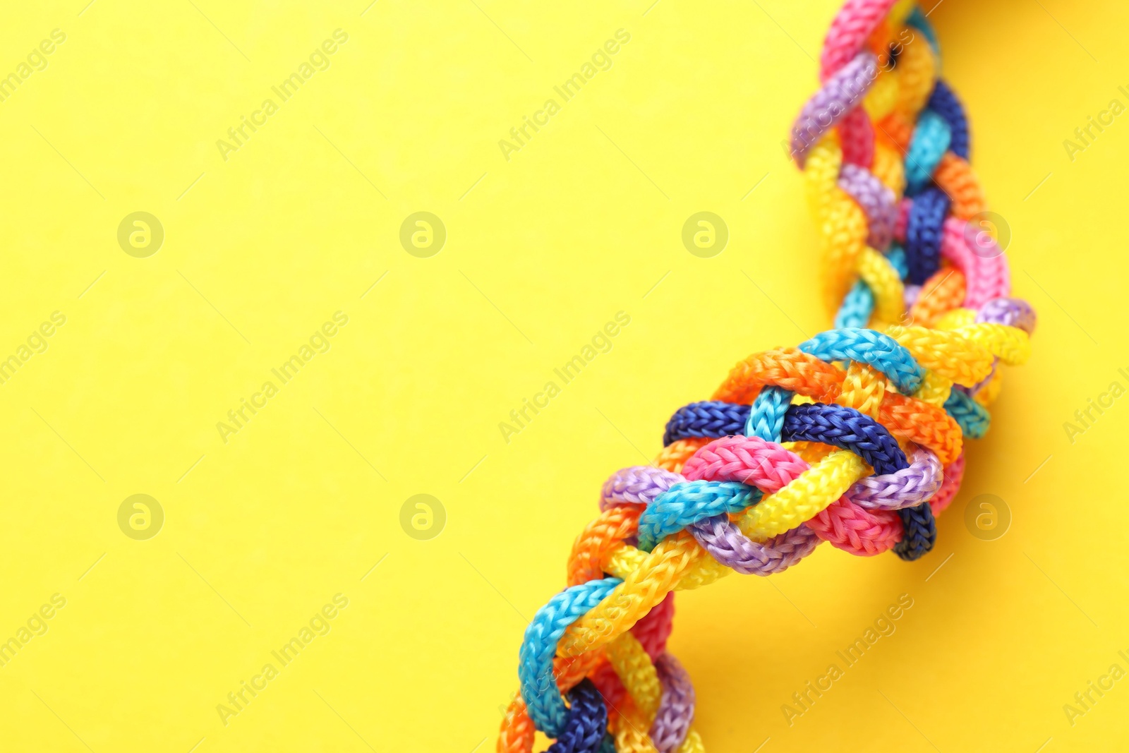 Photo of Braided colorful ropes on yellow background, closeup with space for text. Unity concept