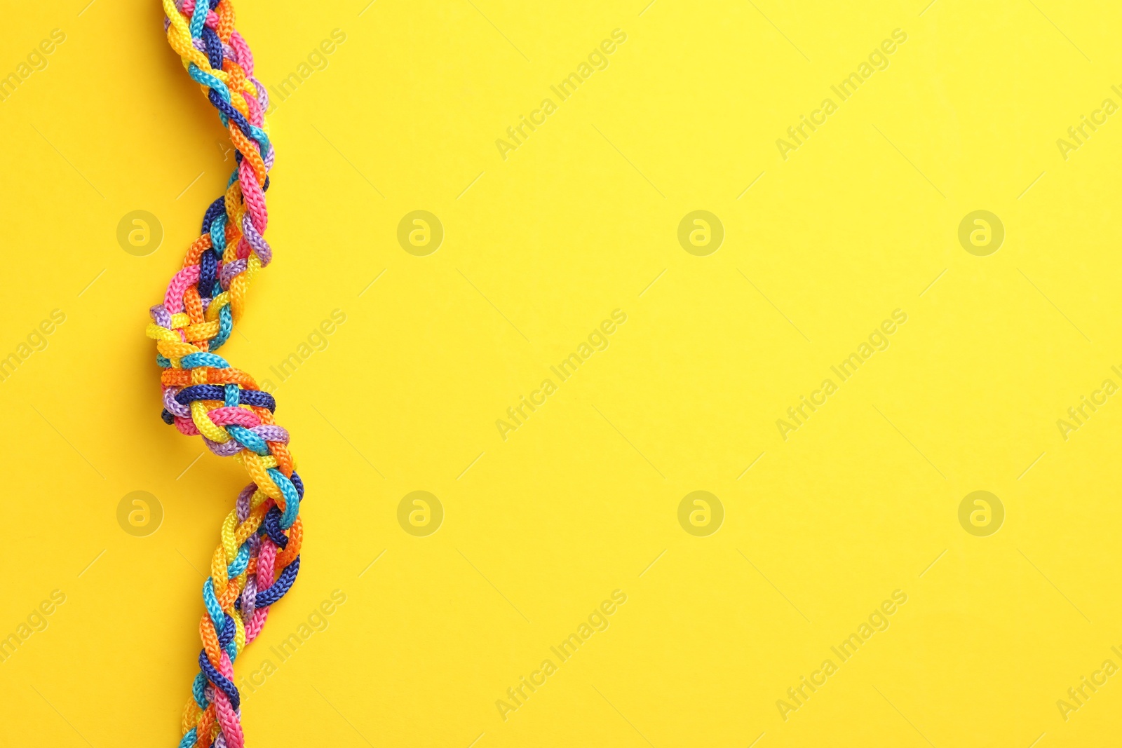 Photo of Braided colorful ropes on yellow background, top view with space for text. Unity concept