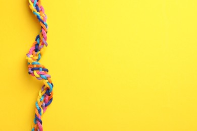 Photo of Braided colorful ropes on yellow background, top view with space for text. Unity concept