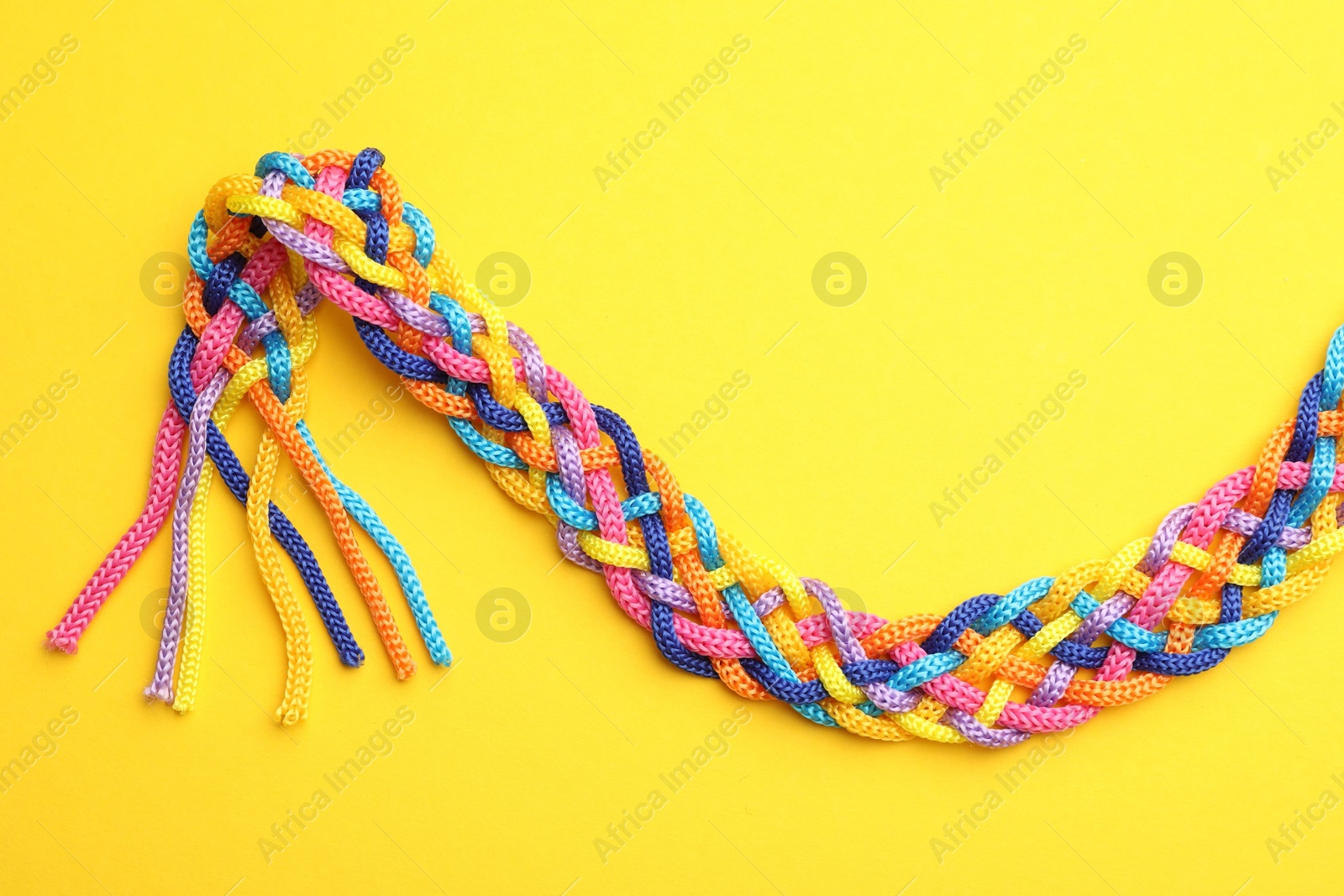 Photo of Braided colorful ropes on yellow background, top view. Unity concept