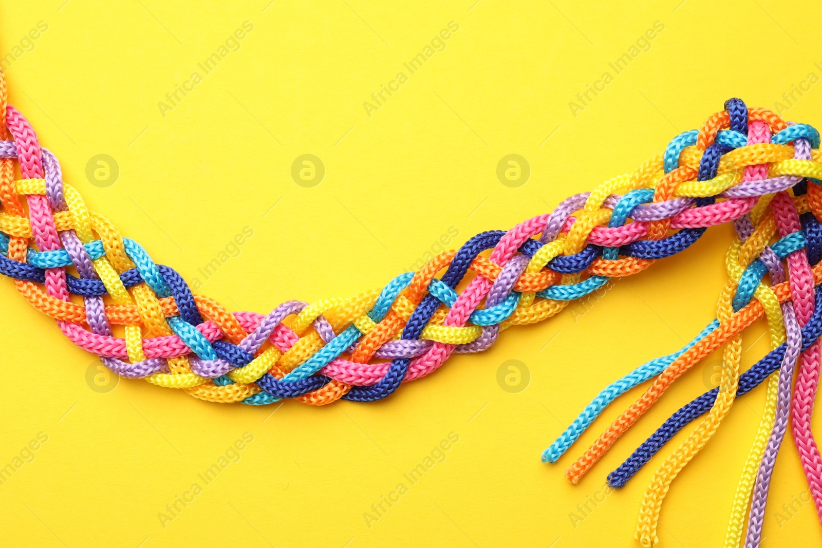 Photo of Braided colorful ropes on yellow background, top view. Unity concept