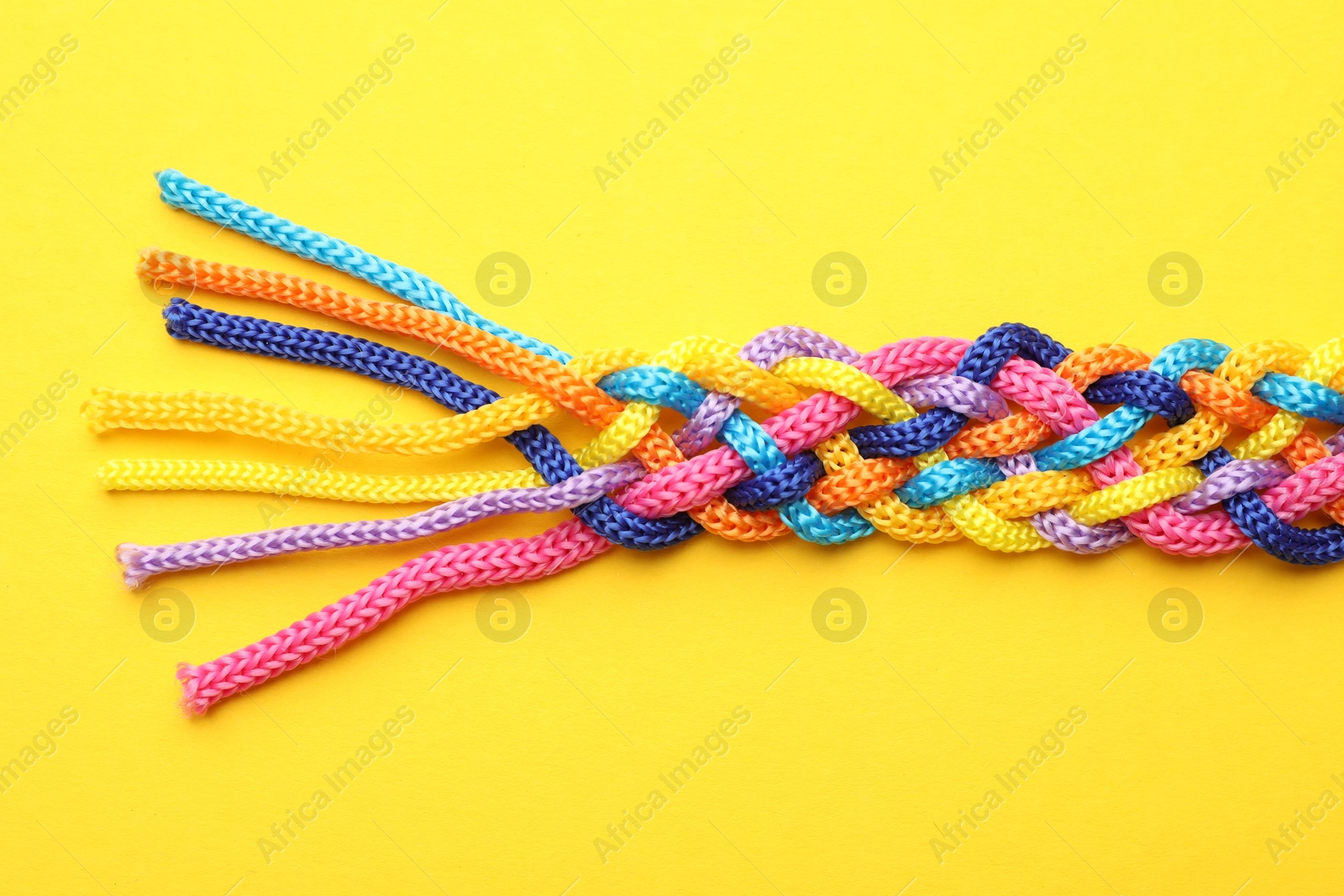 Photo of Braided colorful ropes on yellow background, top view. Unity concept