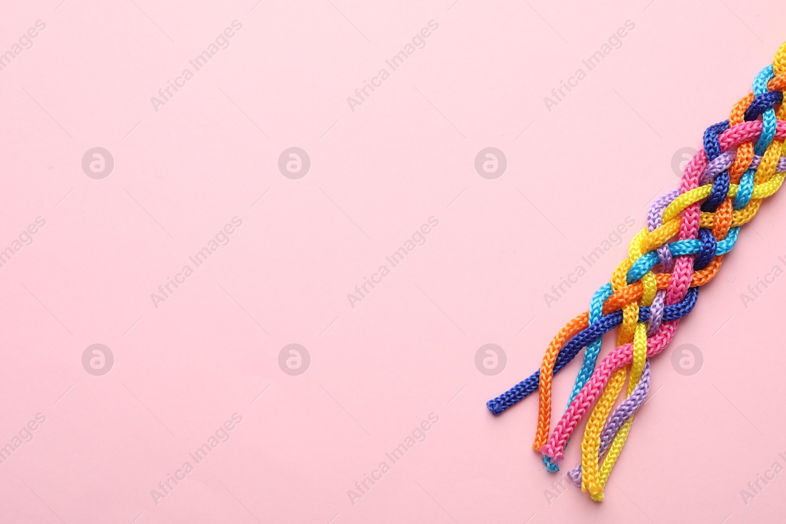 Photo of Braided colorful ropes on pink background, top view with space for text. Unity concept