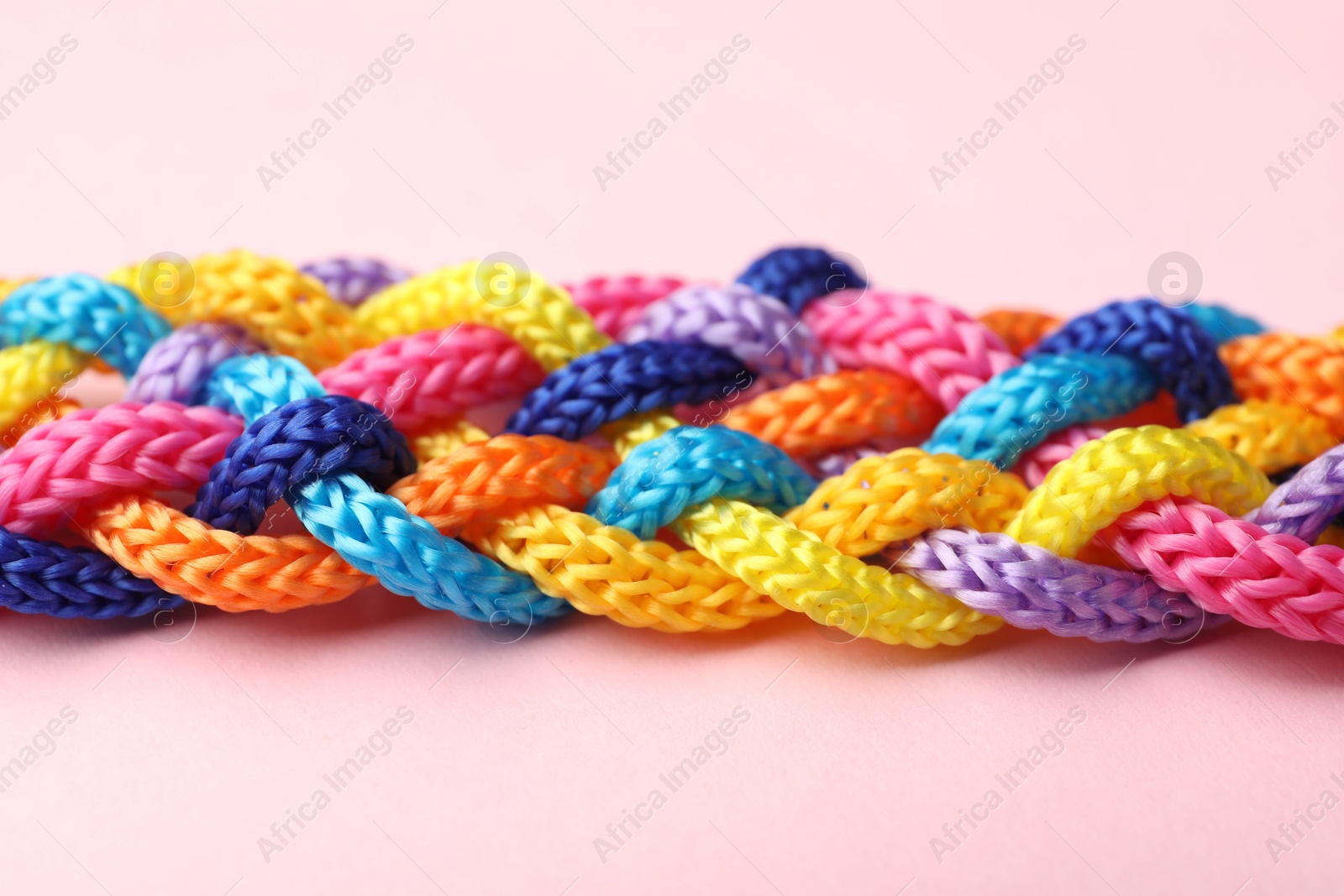 Photo of Braided colorful ropes on pink background, closeup. Unity concept