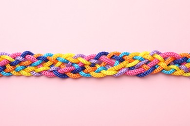 Photo of Braided colorful ropes on pink background, top view. Unity concept