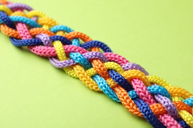 Photo of Braided colorful ropes on green background, closeup. Unity concept