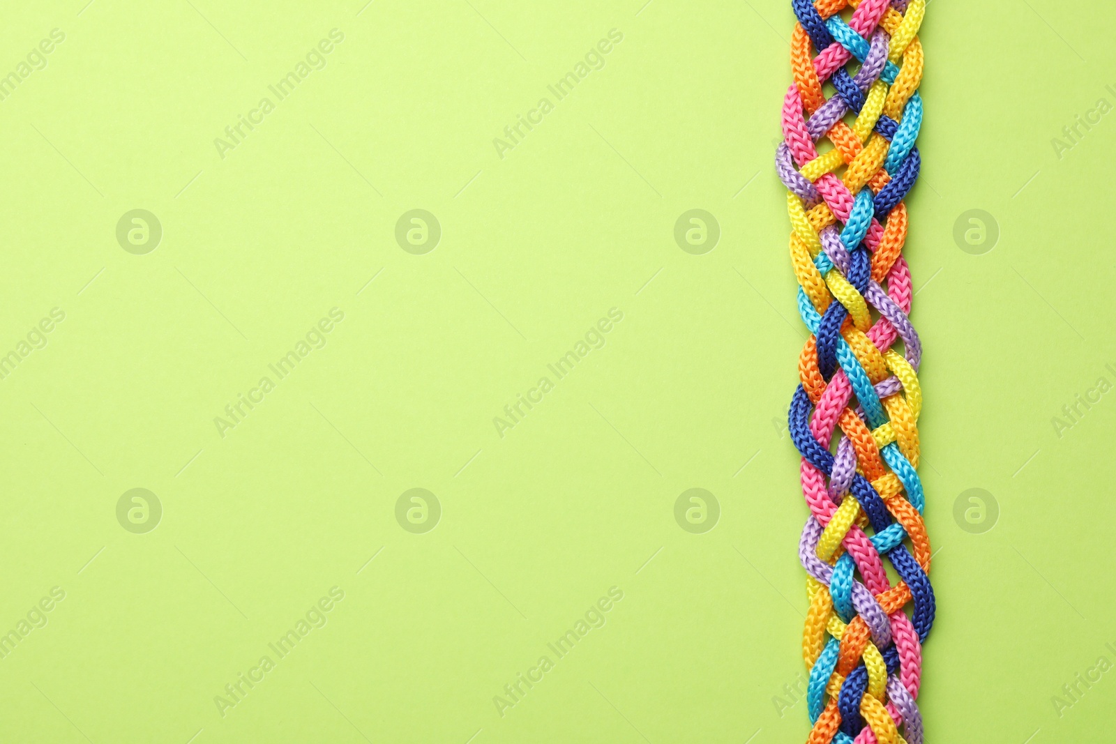 Photo of Braided colorful ropes on green background, top view with space for text. Unity concept