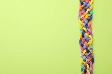 Braided colorful ropes on green background, top view with space for text. Unity concept