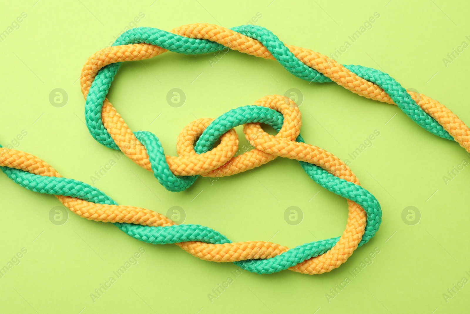 Photo of Braided colorful ropes on green background, top view. Unity concept