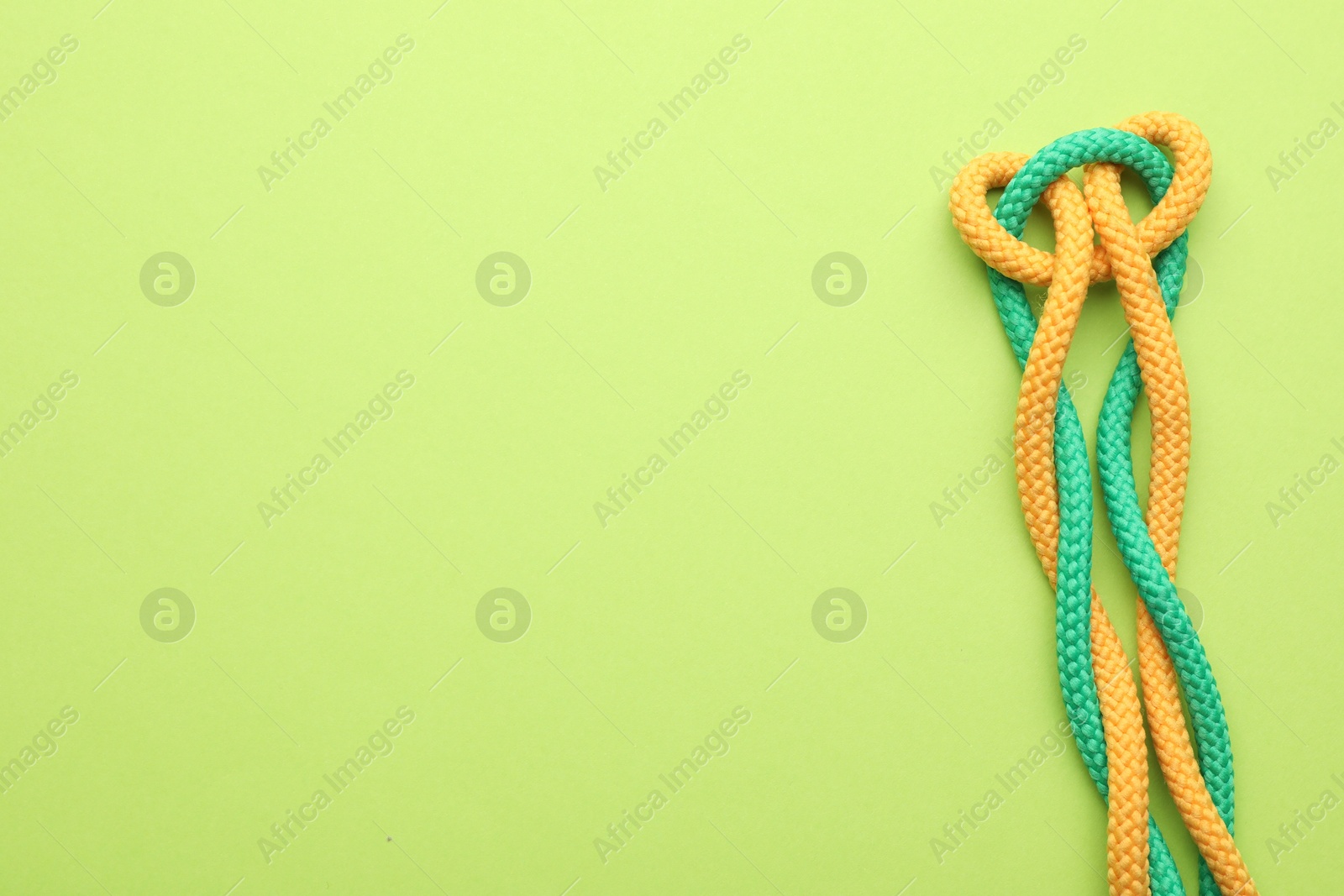 Photo of Colorful ropes tied in knot on green background, top view with space for text. Unity concept