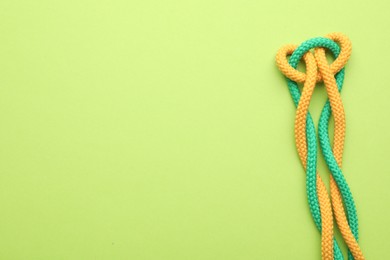 Photo of Colorful ropes tied in knot on green background, top view with space for text. Unity concept