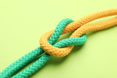 Photo of Colorful ropes tied in knot on green background, closeup. Unity concept