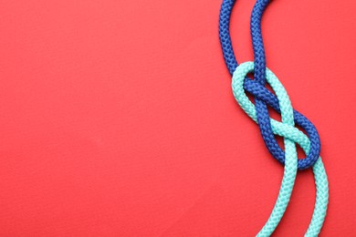 Photo of Colorful ropes tied in knot on red background, top view with space for text. Unity concept