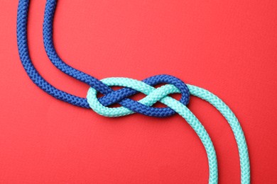 Photo of Colorful ropes tied in knot on red background, top view. Unity concept