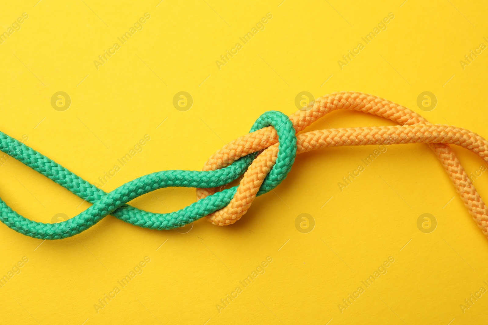 Photo of Colorful ropes tied in knot on yellow background, top view. Unity concept