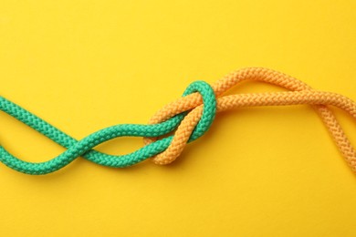 Photo of Colorful ropes tied in knot on yellow background, top view. Unity concept