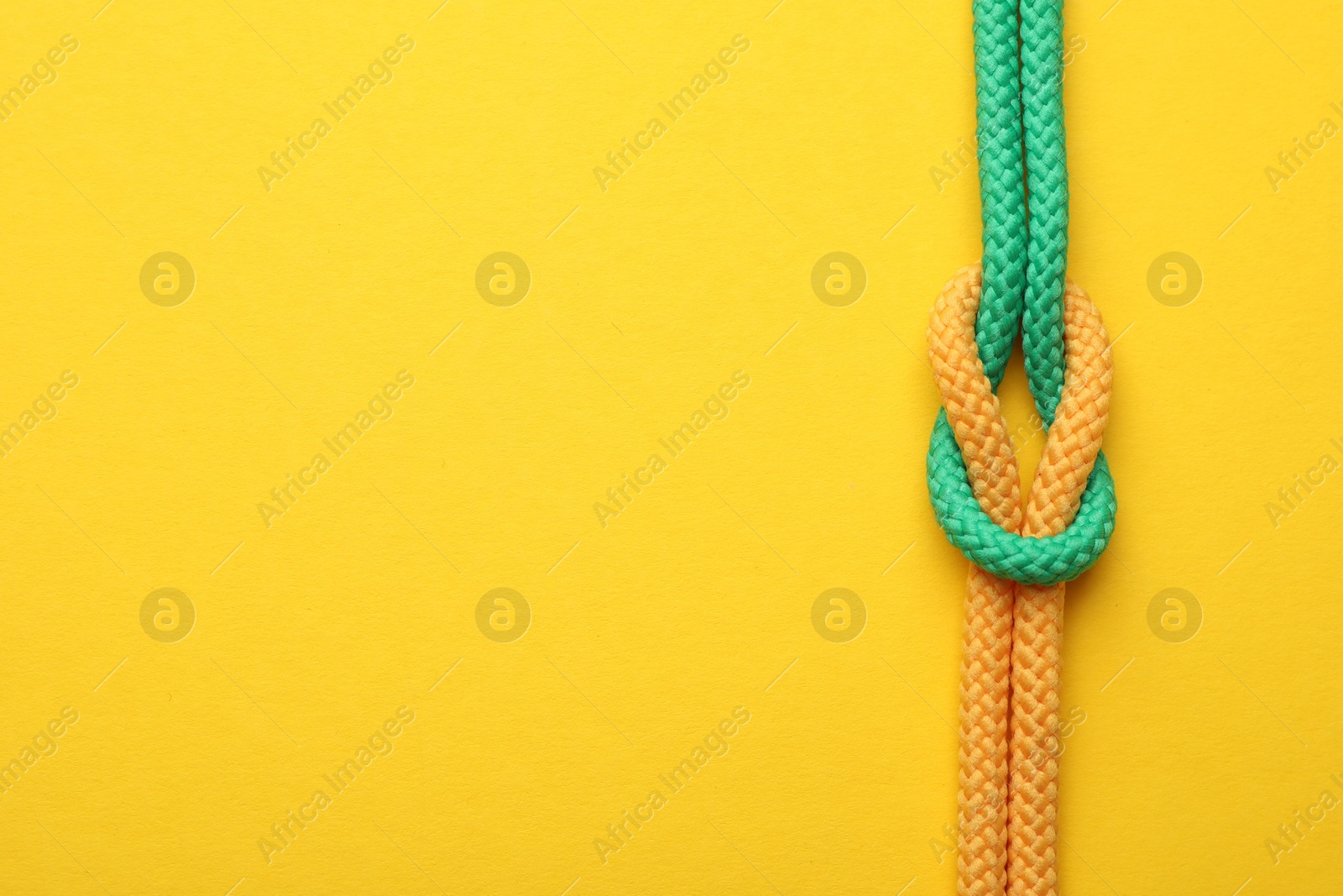 Photo of Colorful ropes tied in knot on yellow background, top view with space for text. Unity concept