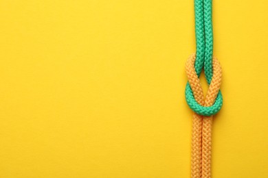 Photo of Colorful ropes tied in knot on yellow background, top view with space for text. Unity concept