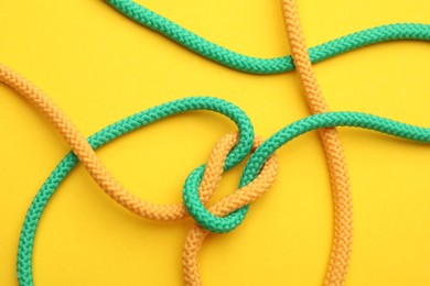 Photo of Colorful ropes tied in knot on yellow background, top view. Unity concept